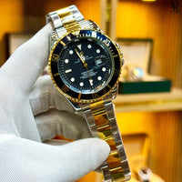 Gold and silver watch with black dial held by a gloved hand against a blurred background