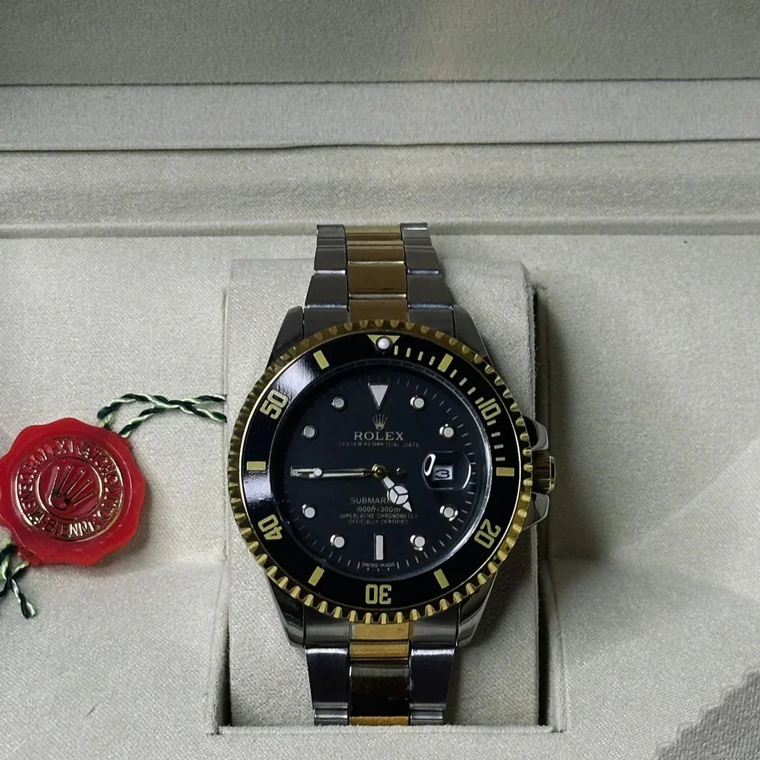 Rolex watch with black dial and gold accents on a gray surface with a red logo.