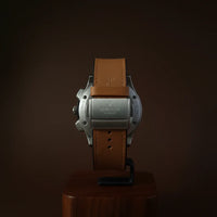 Watch with brown leather strap on a wooden stand against a dark background