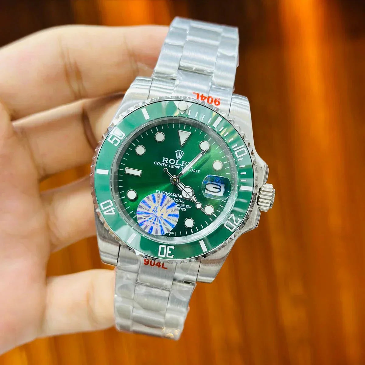 Rolex watch with green dial and silver metal bracelet held by a hand against a blurred background